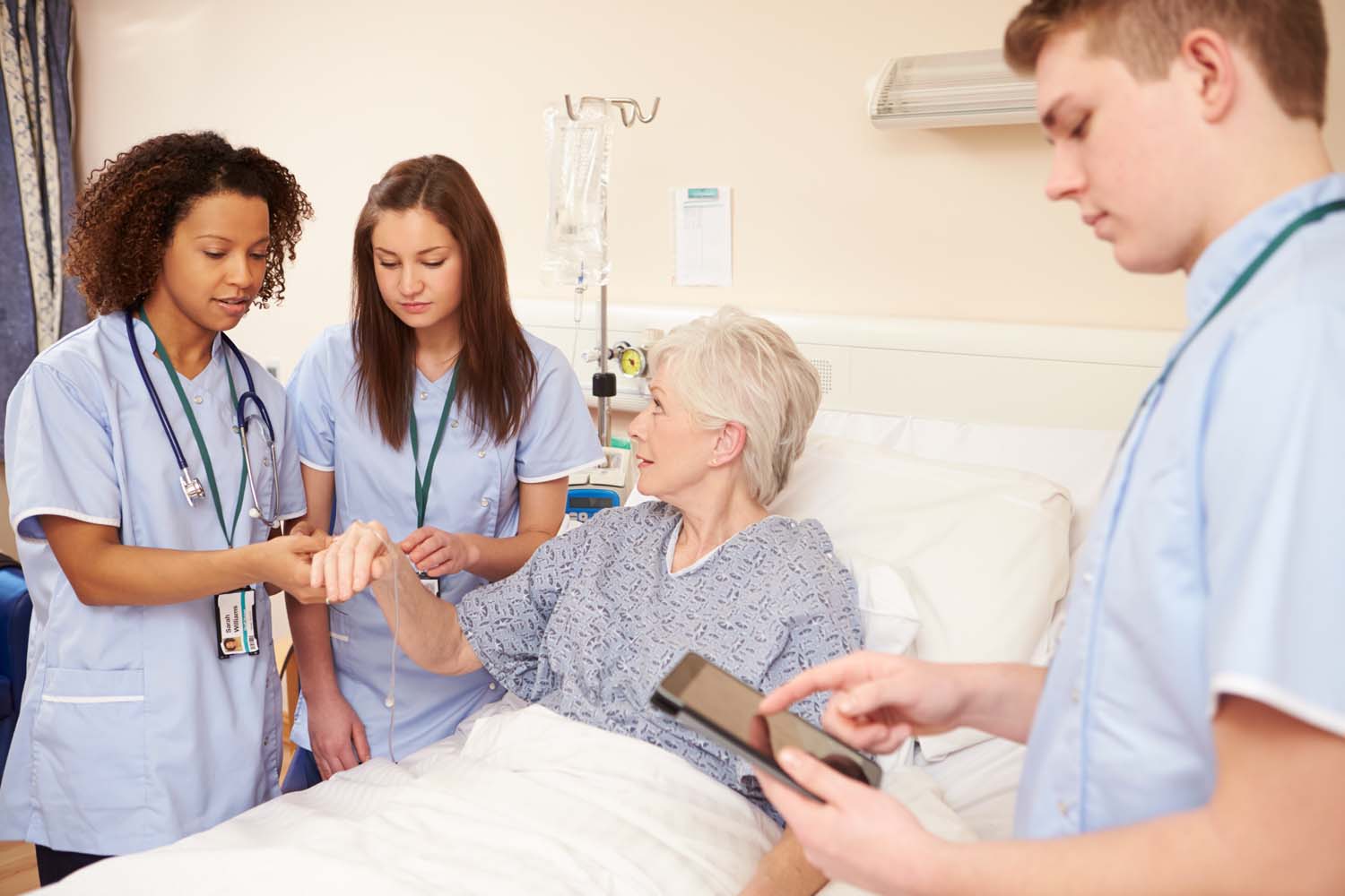 Trainee Nursing Staff By Female Patient's Bed In Hospital